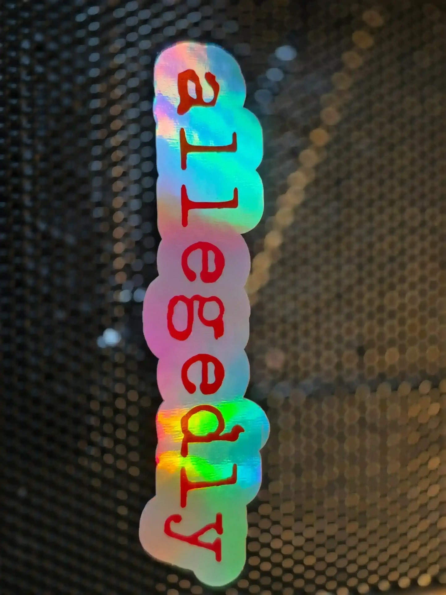 Holographic sticker with 'allegedly' in red on Cady Creations dark humor background