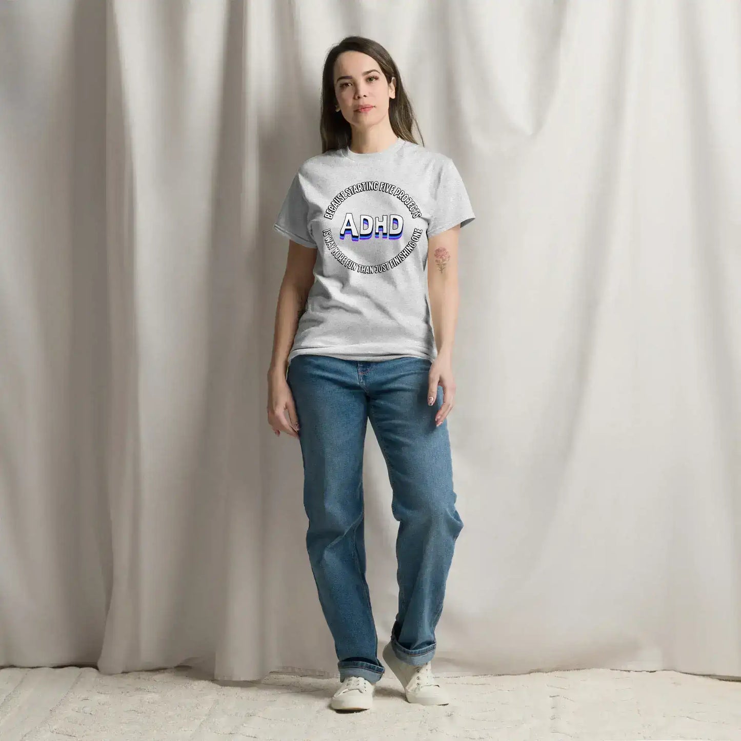 Woman wearing Cady Creations graphic ADHD tee and blue jeans, standing indoors with neutral backdrop.