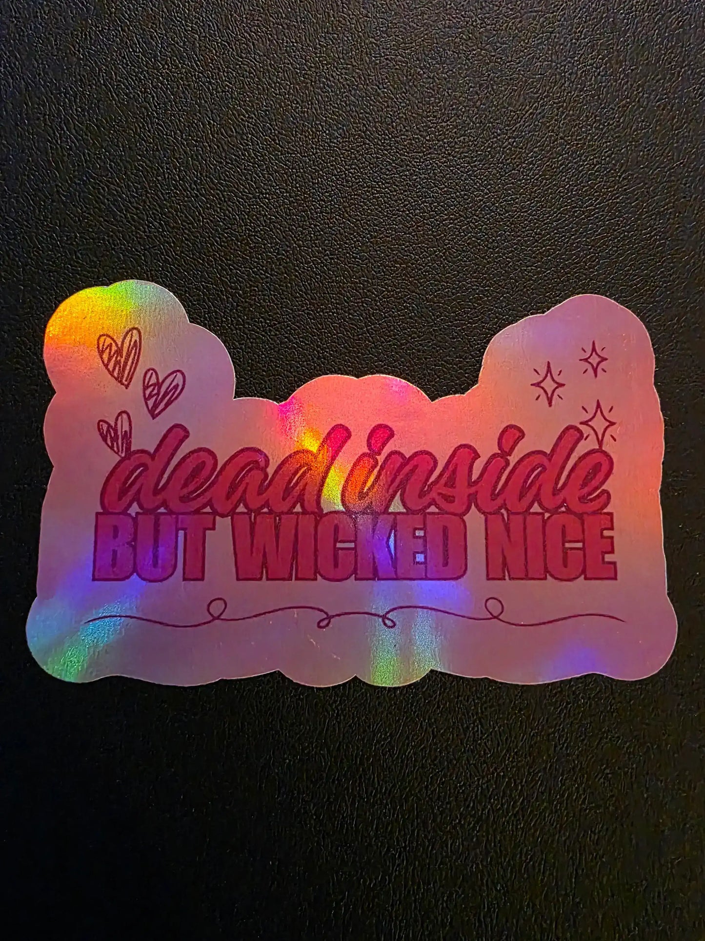 Holographic sticker with text 'dead inside but wicked nice' on a dark background