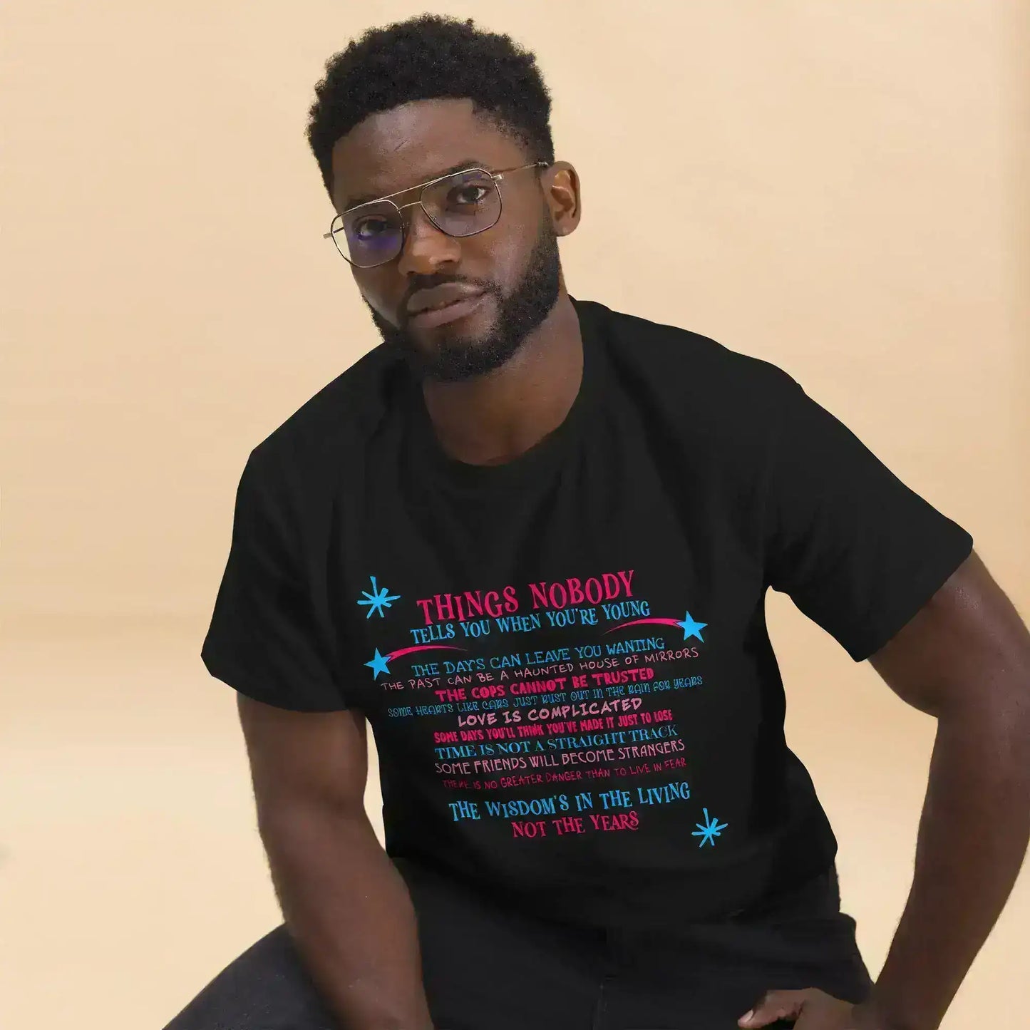 Man wearing Cady Creations unisex black graphic tee with colorful text, beige background