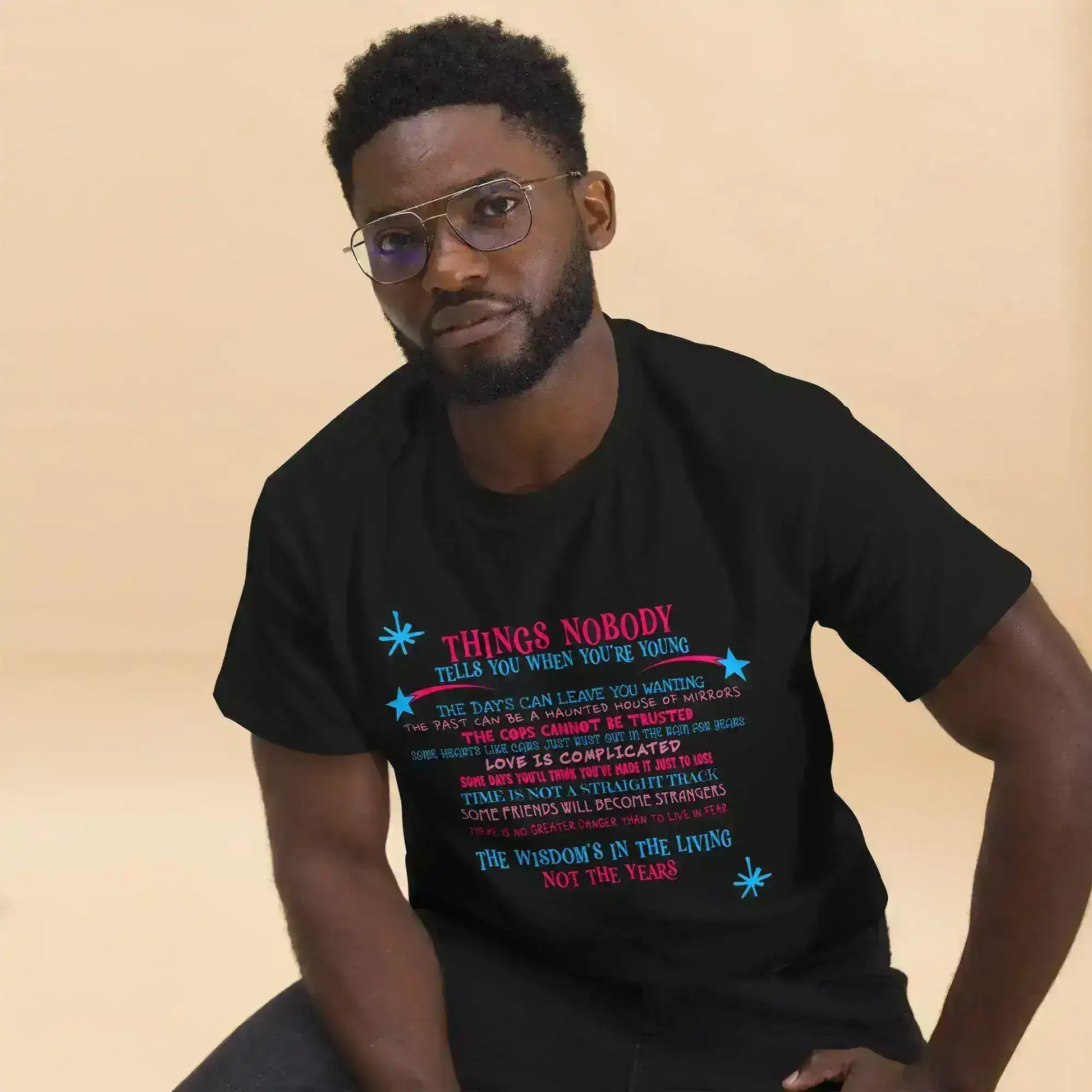 Man wearing Cady Creations unisex black graphic tee with colorful text, beige background