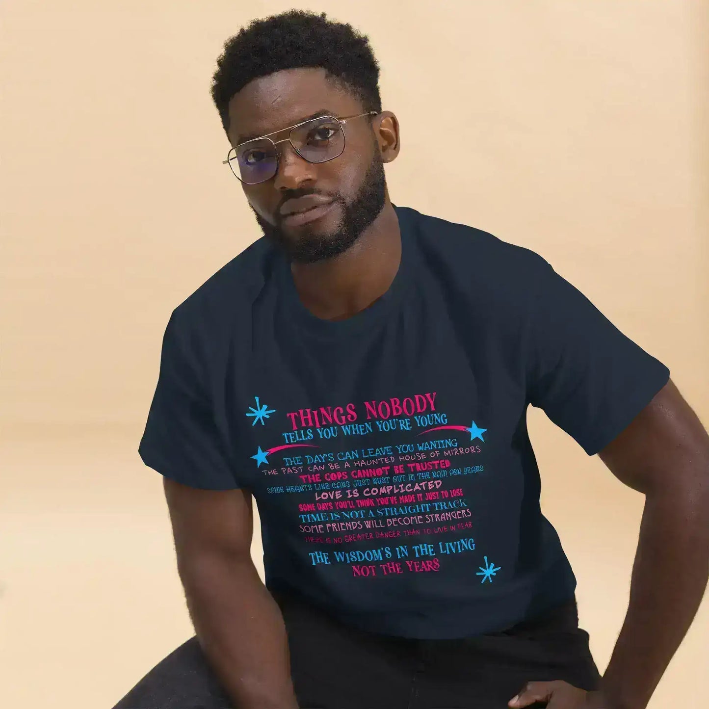 Man wearing Cady Creations unisex navy graphic tee with colorful text, seated indoors
