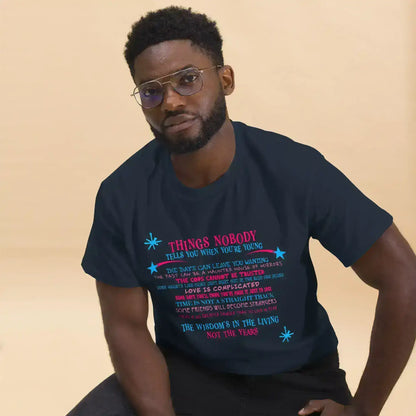 Man wearing Cady Creations unisex navy graphic tee with colorful text, seated indoors