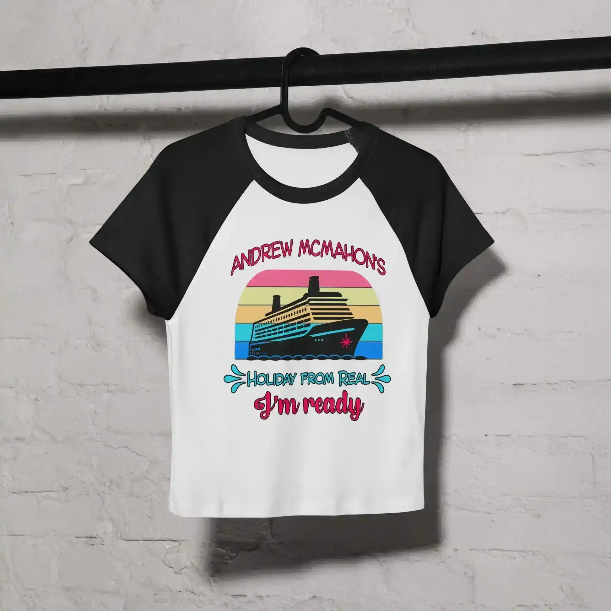 Women's black and white raglan baby tee with cruise ship graphic and colorful text, hung on hanger