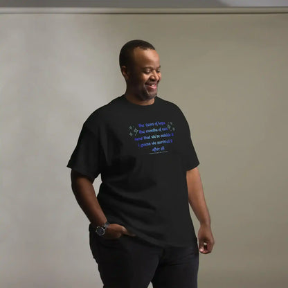 Smiling man wears a black Cady Creations graphic tee with blue text, hands in pockets, neutral background.