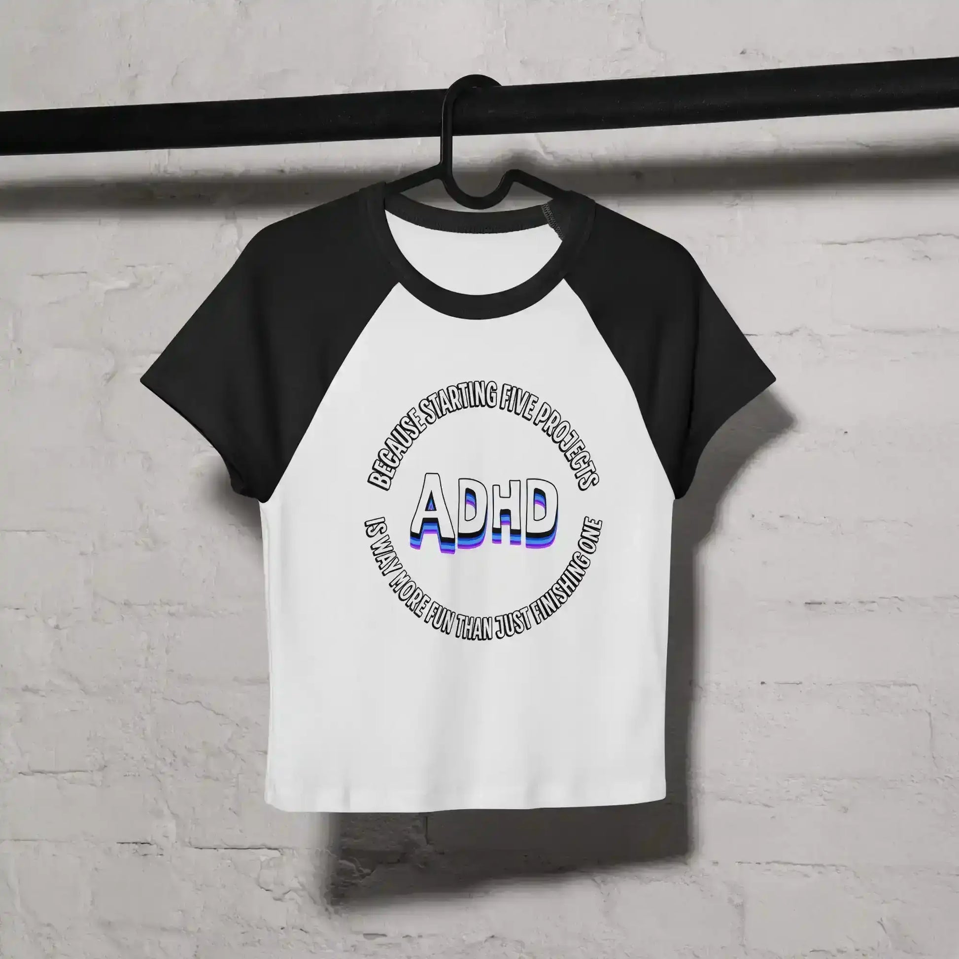 White and black women's raglan baby tee with ADHD graphic text, hanging on a black rod