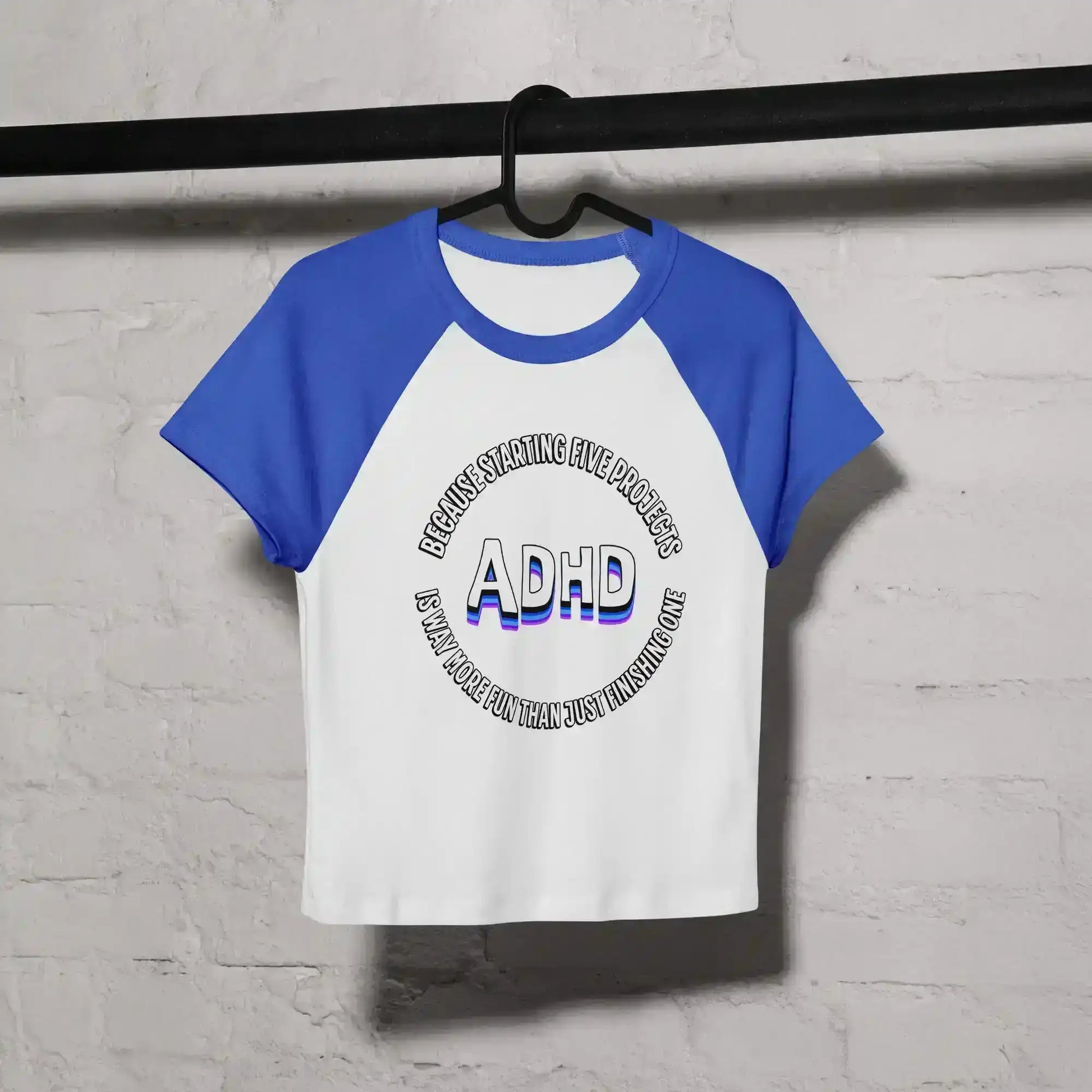 White and blue women's raglan baby tee with ADHD graphic text, hanging on a black rod